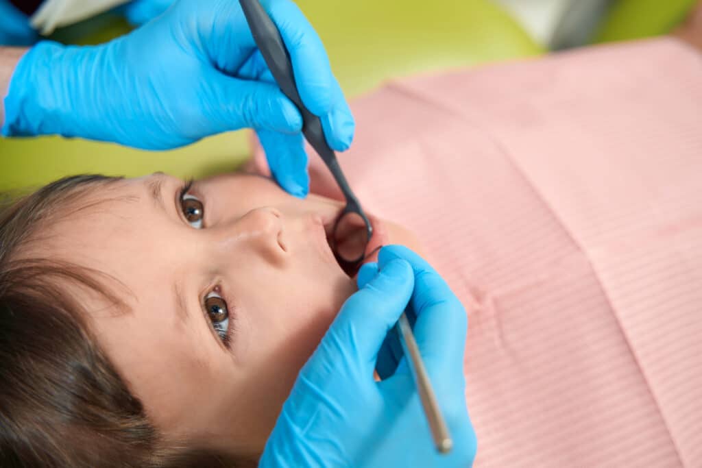 pediatric dentist inspecting child's teeth condition for cavities treatment.